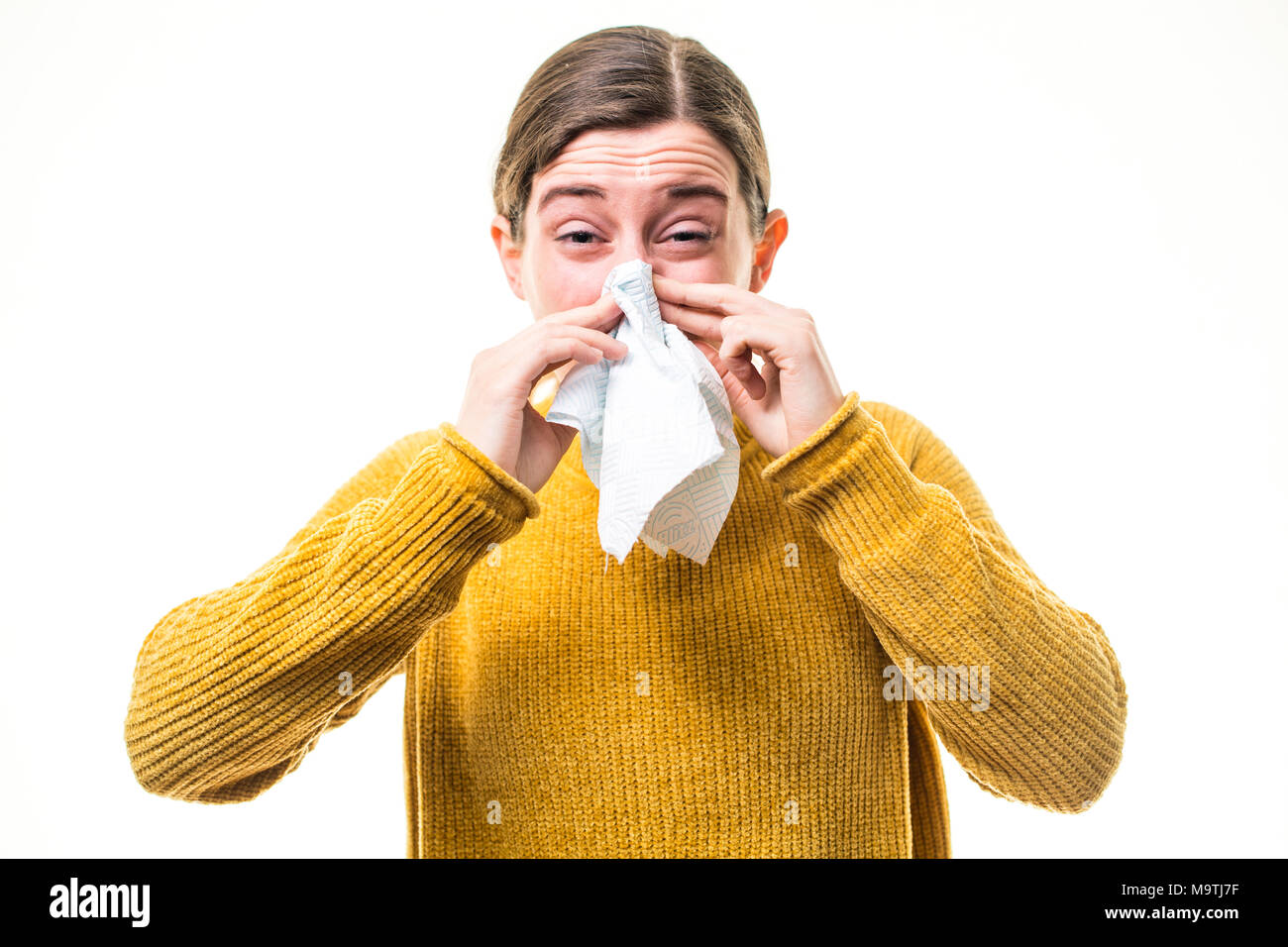 A young Caucasian woman girl wearing a yellow jumper sweater,  suffering from cold or influenza, sneezing ,  blowing her nose into a paper handkerchief, UK Stock Photo