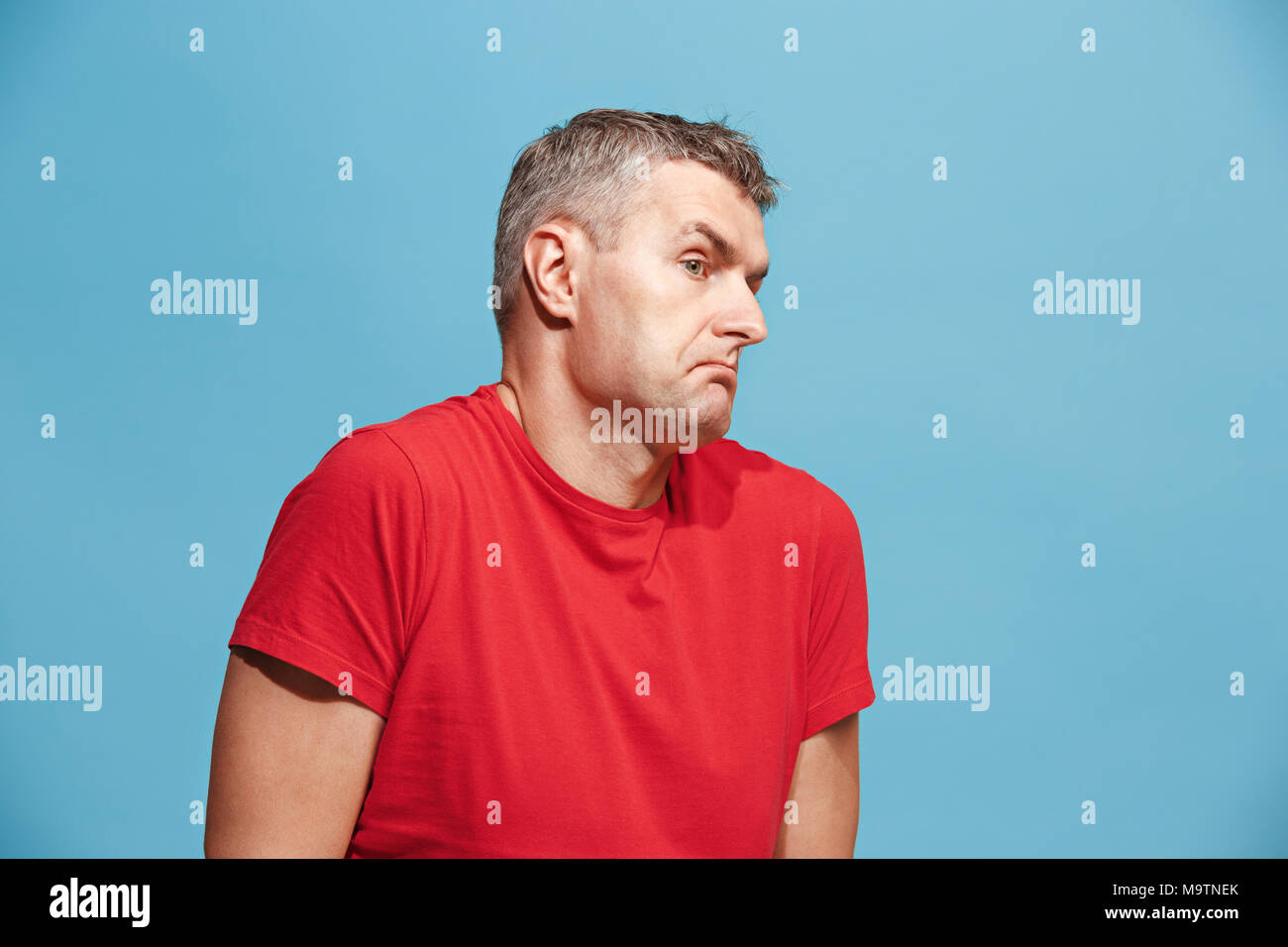 Suspiciont. Doubtful pensive man with thoughtful expression making choice against blue background Stock Photo