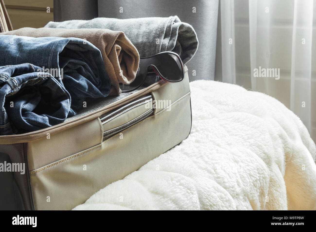 Open door and open suitcase with clothes. Stock Photo