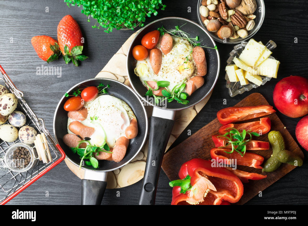 English health breakfast for two. Fried eggs with sausages in a frying pan with spices and fresh vegetables. Stock Photo