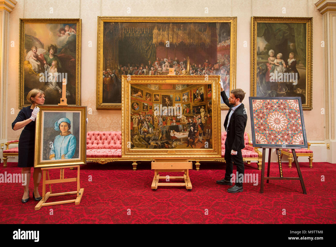 Royal Collection staff adjust (front row, left to right) an oil sketch 'HM the Queen, 1972-73' by Michael Noakes, 'The Tribuna of the Uffizi, 1772-77' and a Moroccan inspired painting by Natasha Mann during the press preview of the Prince and Patron exhibition at Buckingham Palace, London, which will mark the 70th birthday of the Prince of Wales this year. Stock Photo