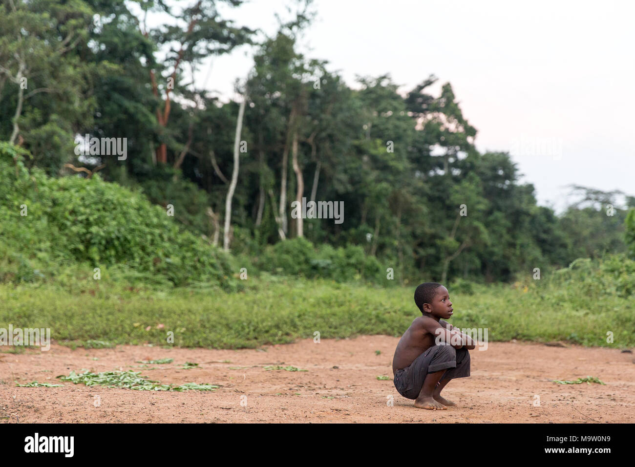 A young boy rests from playing football in Guiapleu, western Cote d'ivoire. Guiapleu is a tiny village made up of many nationalities and religions. There are residents that are Ivorian, Guinean, Liberian, Burkinabe and Malian many of which have fled persecution or war. There is both a Catholic and Protestant church as well as a Mosque. Stock Photo