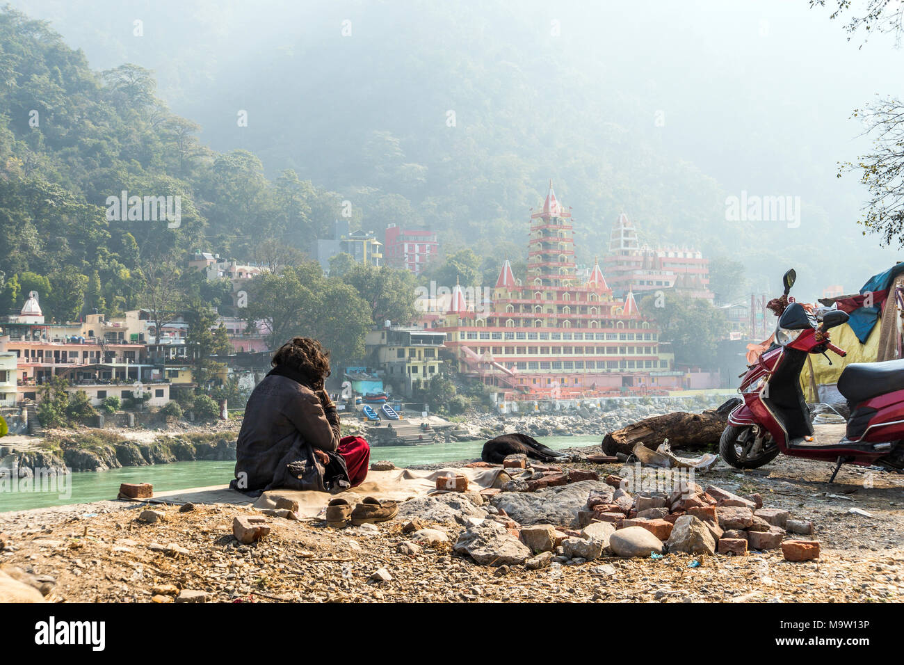 poor man sits on the banks of the Ganges river and looks towards the temple Tera Manzil Temple. Morning prayer before the Holy place. Meditation in Ri Stock Photo