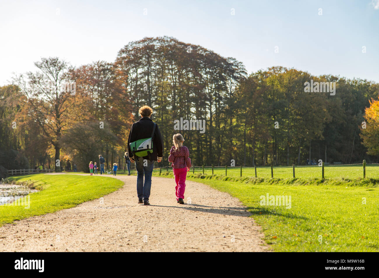 Man with bag walking with little girl on gravel road next to a forest. Stock Photo