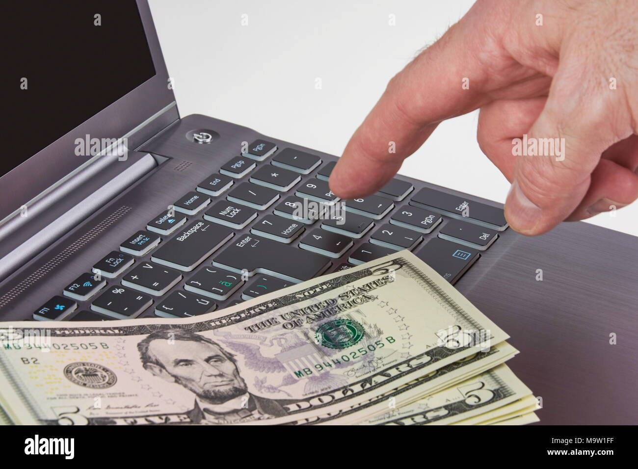 Silver laptop with dollar bills and hands typing on a keyboard, on white background Stock Photo