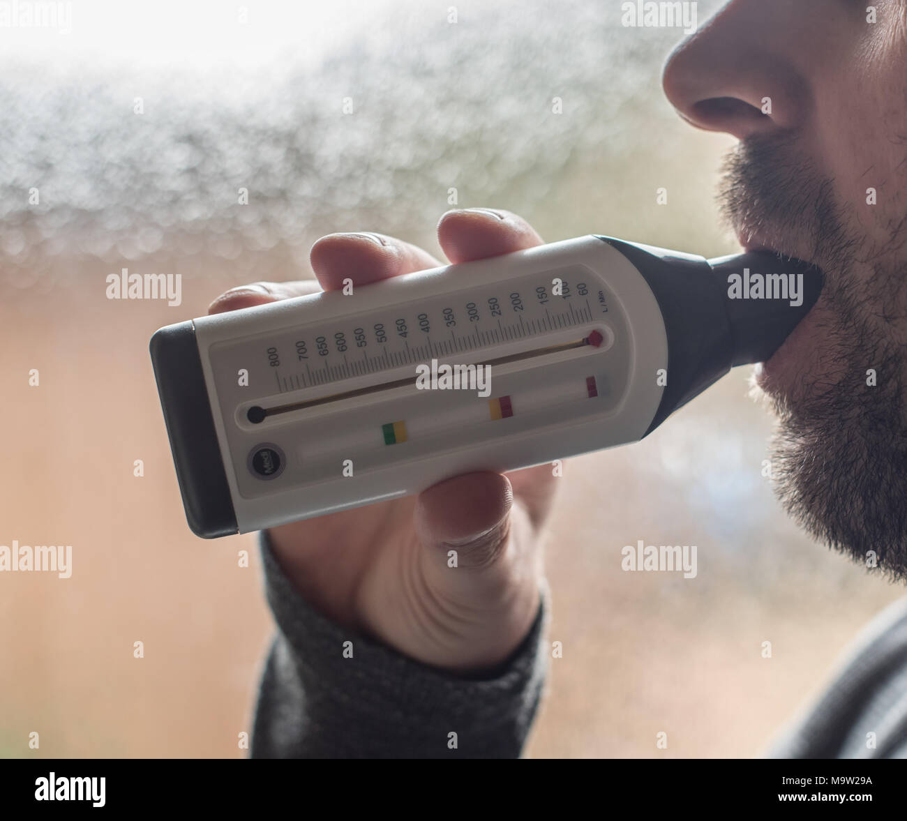 Man blowing into a peak flow meter to check from asthma severity Stock