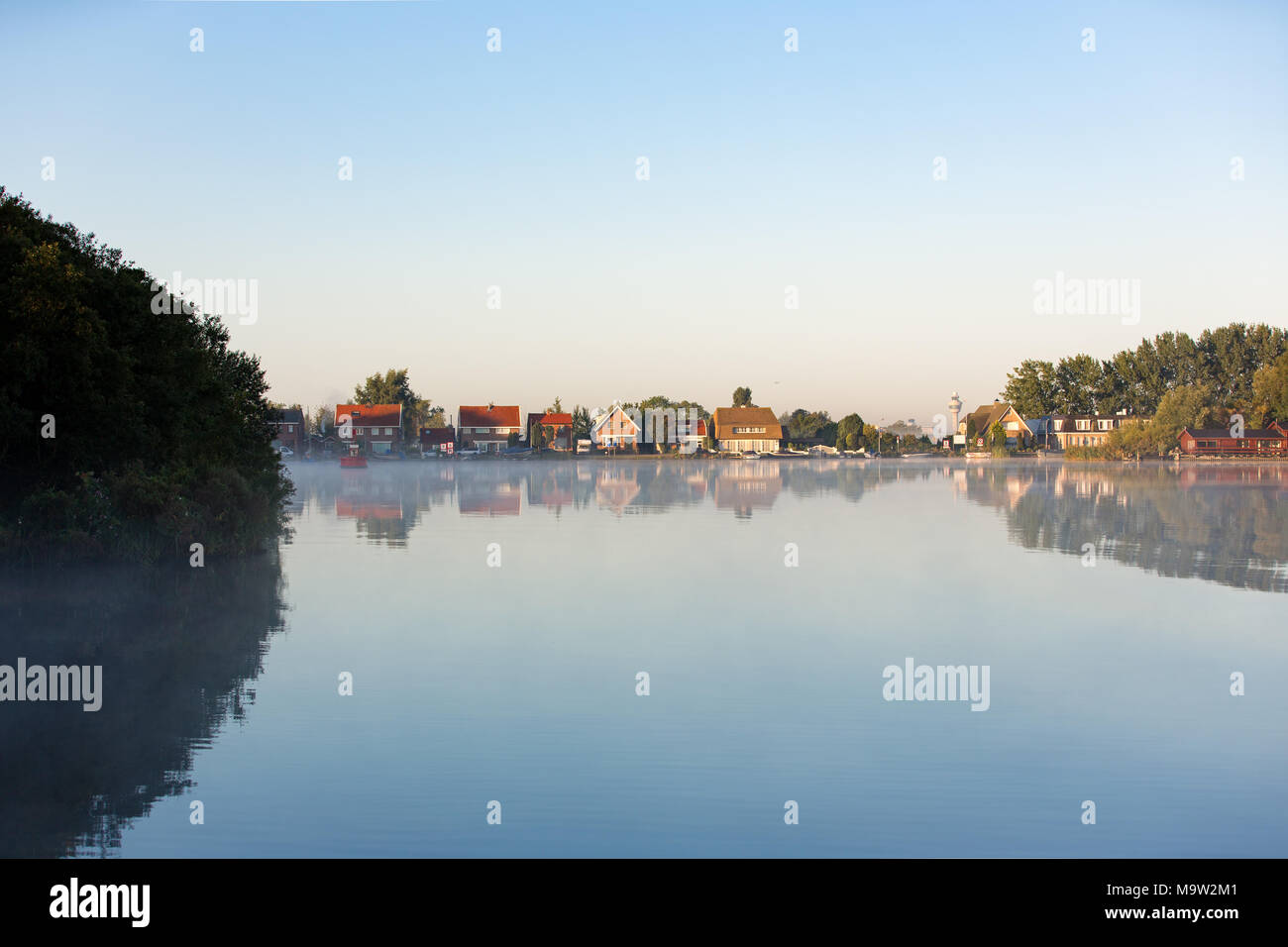 Airtrafic tower and houses on a windless and foggy morning at lake 'Nieuwe Meer' in Amsterdam the Netherlands. Stock Photo