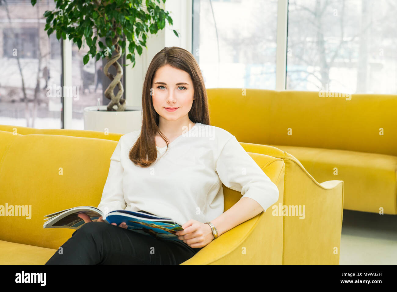 Portrait of young girl looking at camera, sitting on bright yellow sofa ...