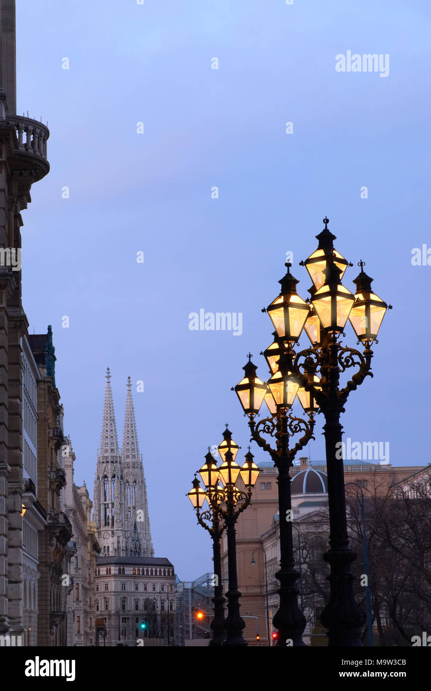 Ornate historical lamp posts outside Rathaus Vienna, or Vienna Town Hall in the evening. Votivkirche sphires are in the background. Stock Photo