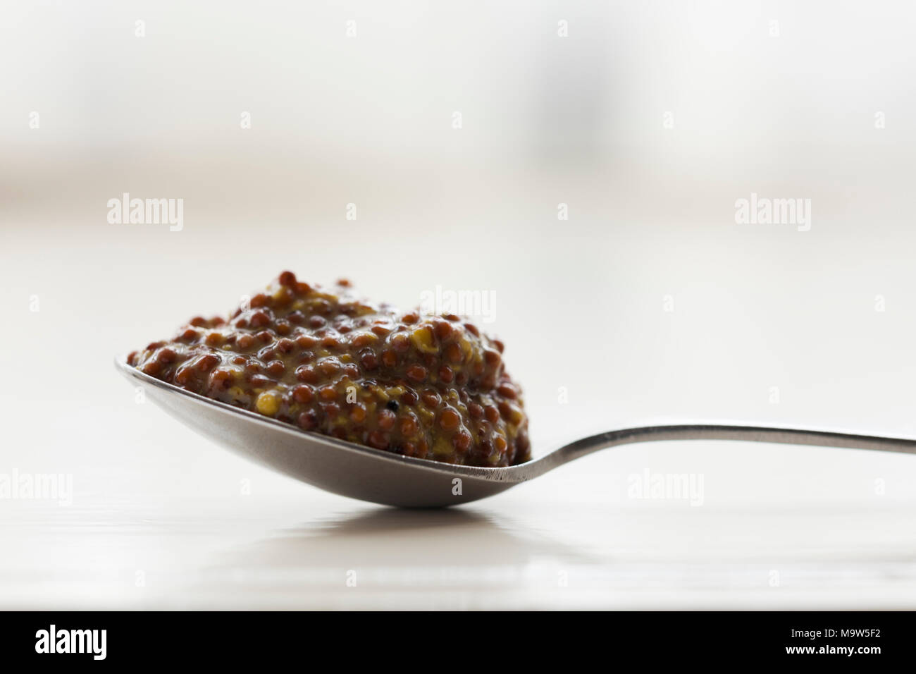 A heaped teaspoon of wholegrain mustard shot in natural light with very shallow depth of field. Stock Photo