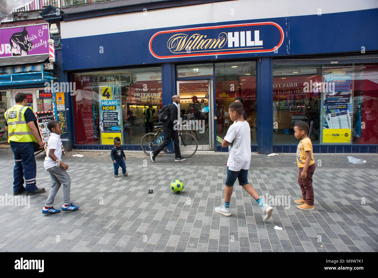 London. Children play football in front of William Hill bet shop, Brixton. United Kingdom. Stock Photo