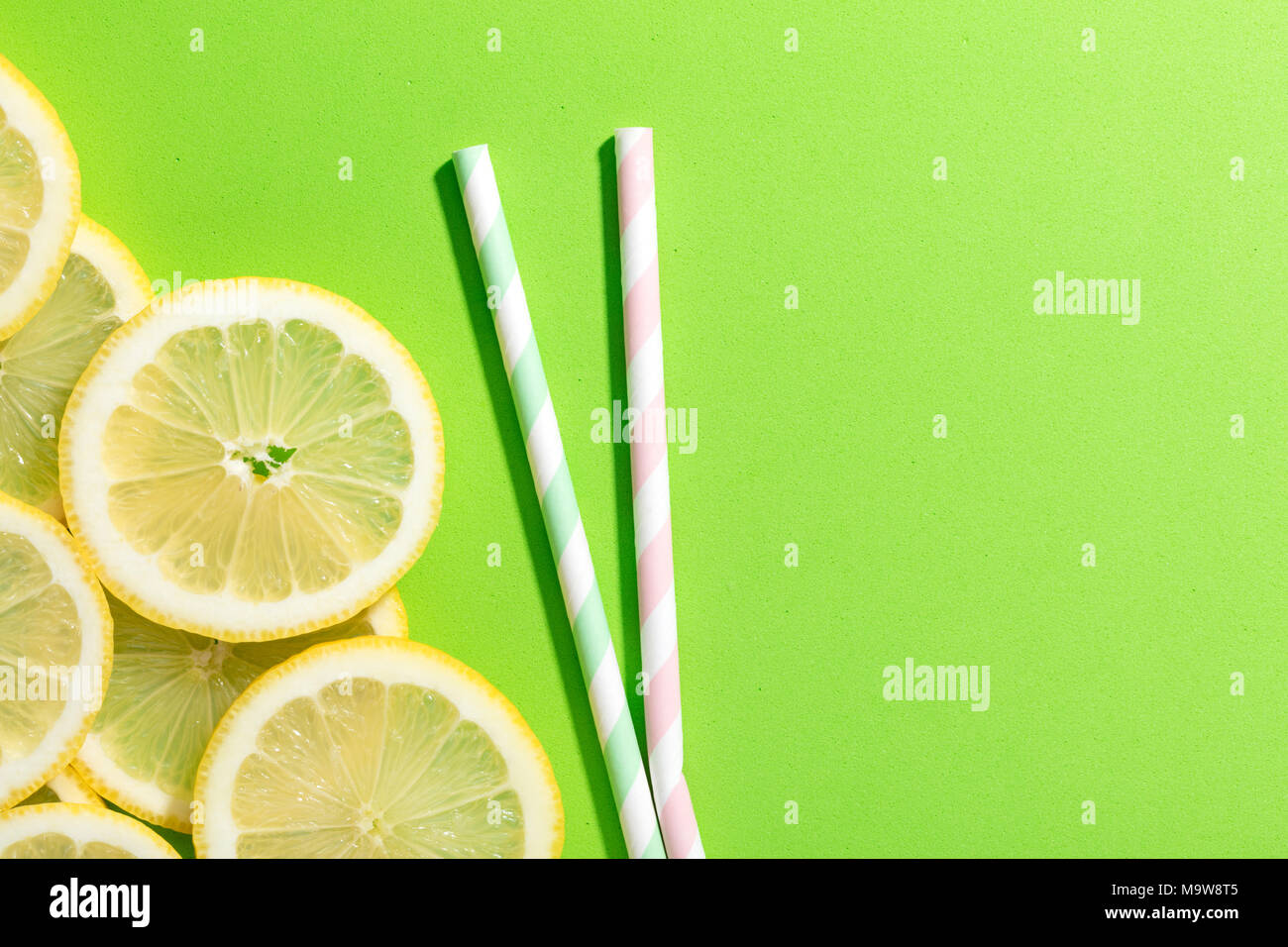 slices of lemon on green colored background with two striped straw Stock Photo