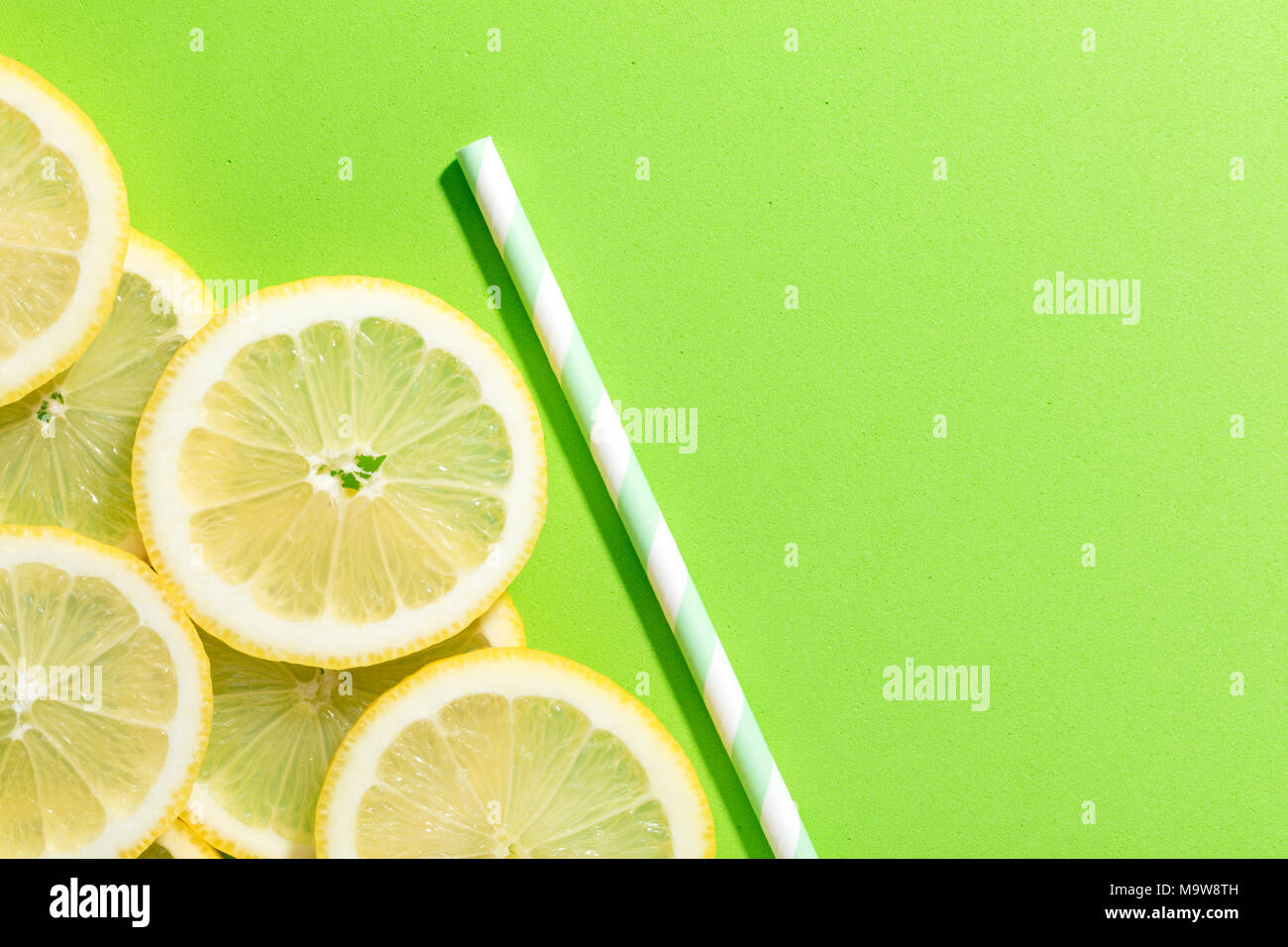 slices of lemon on green colored background with an striped straw Stock Photo