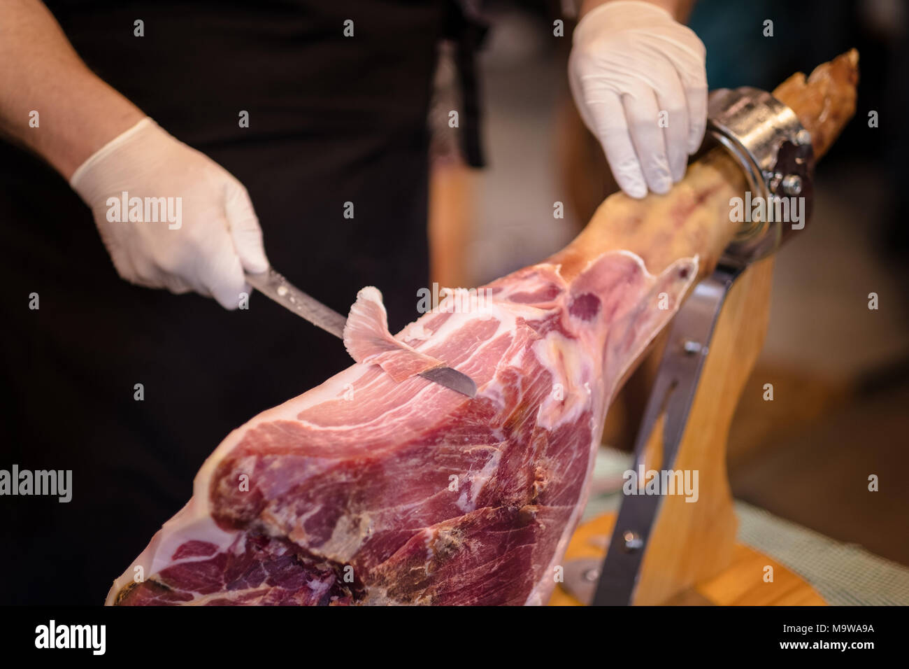 A front leg of Serrano ham also known as Spanish Iberian ham or Pata Negra mounted on a wooden stand with a butcher cutting slices of it Stock Photo