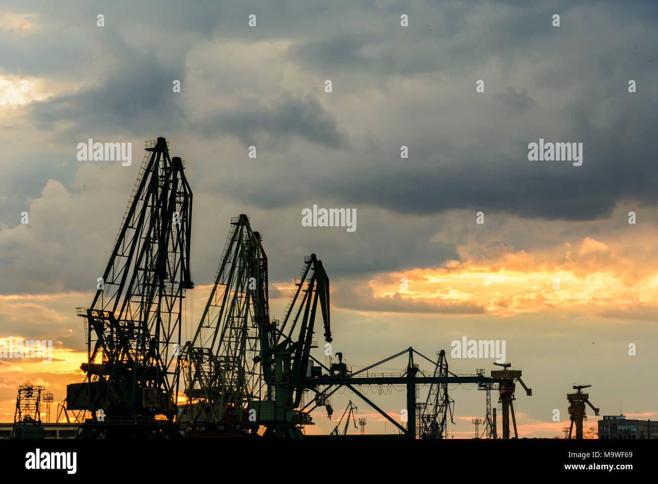 Silhouette of port cranes against a dramatic sky at sunset Stock Photo ...