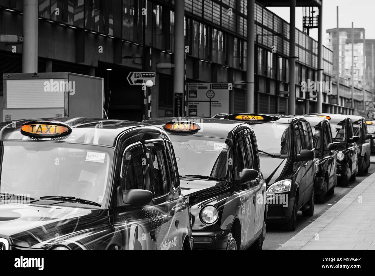 A queue of London black cab taxis in a row at a taxi rank, waiting to pick up passengers near Kings Cross station with for hire light illuminated Stock Photo