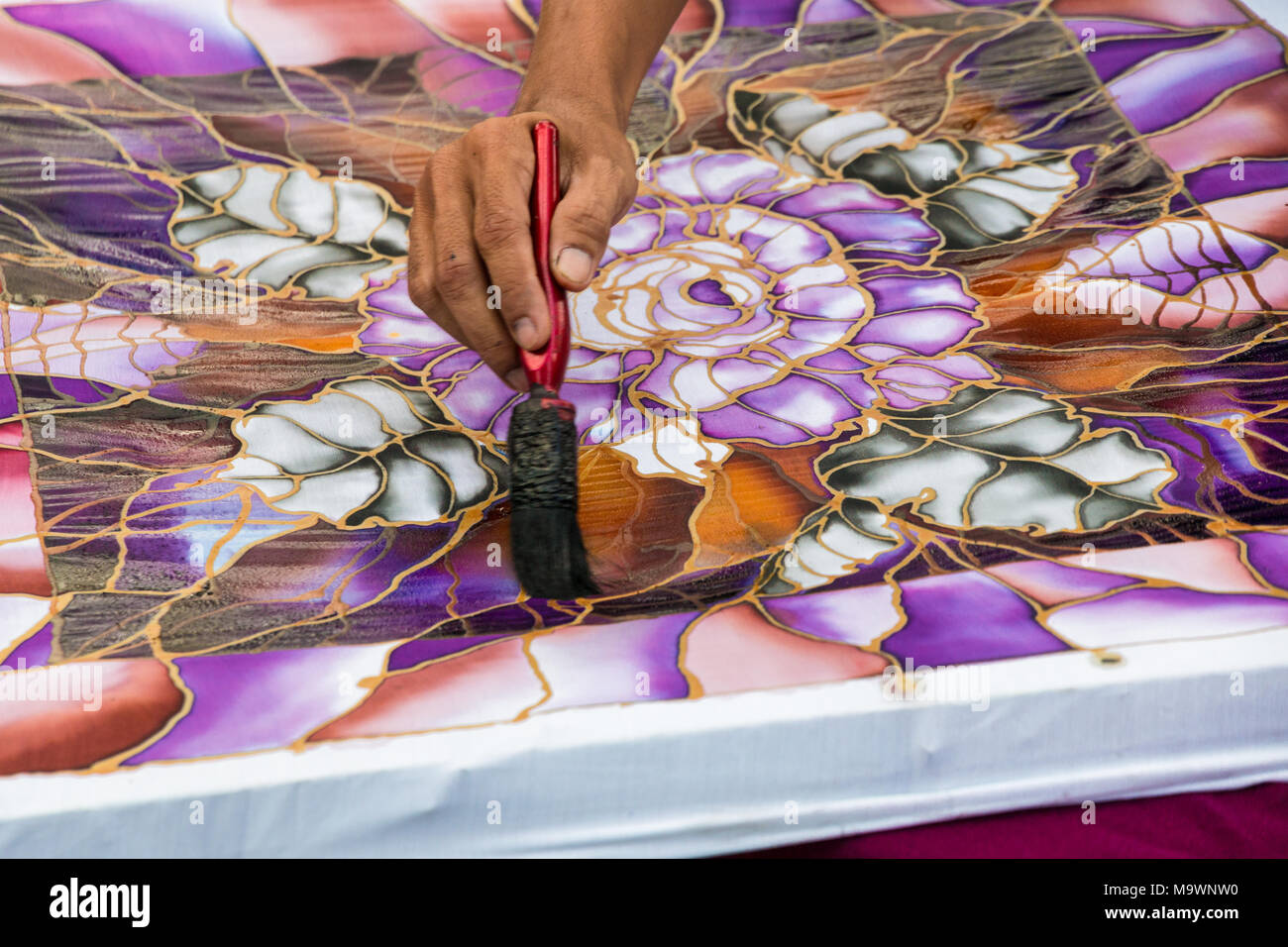 Close-up of a Malaysian batik craftsman teaching how to brush paint colours to a fabric with the popular motif of leaves and flowers. Stock Photo
