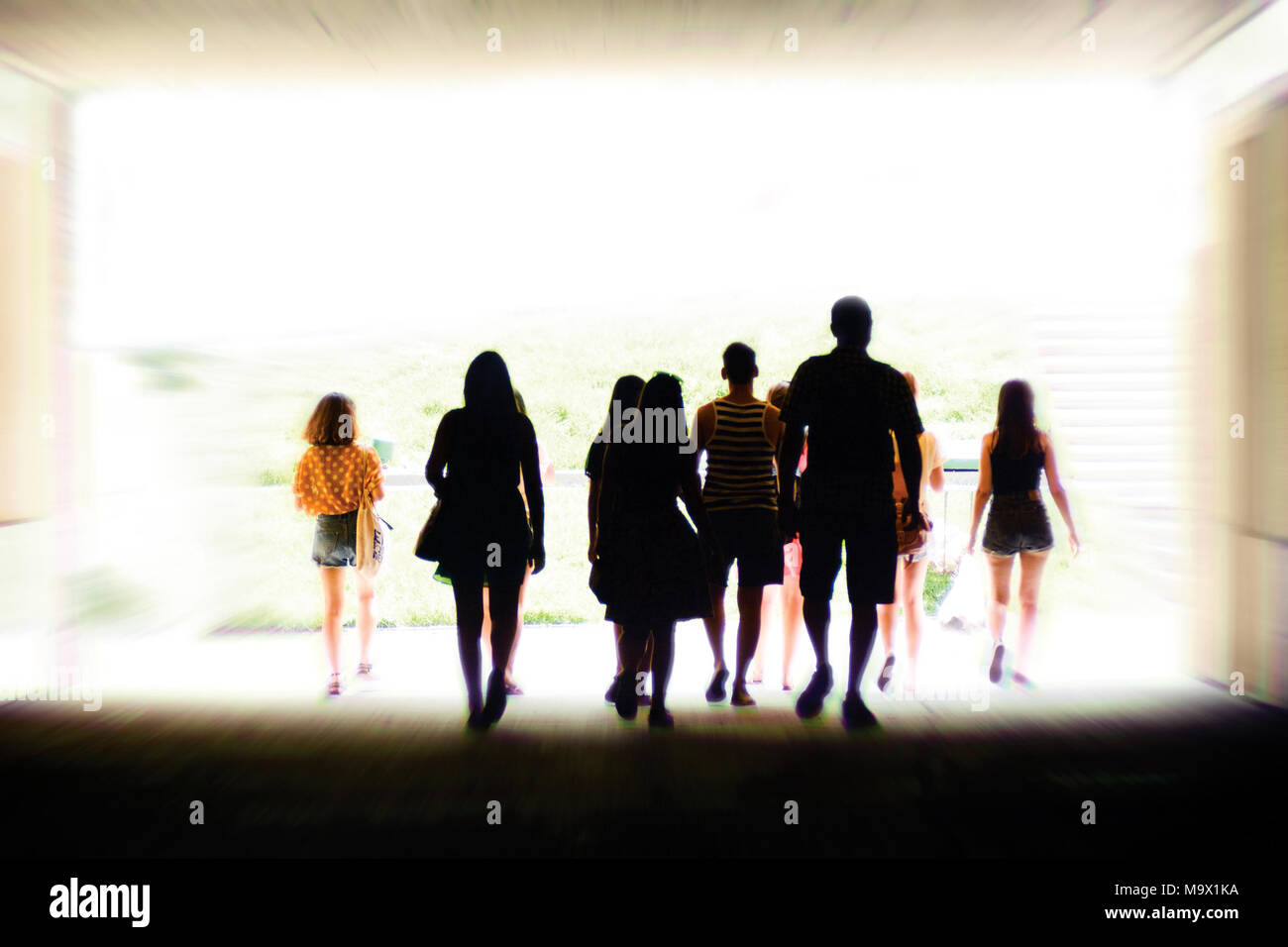 Group of everyday people walking away from shadow into bright light Stock Photo