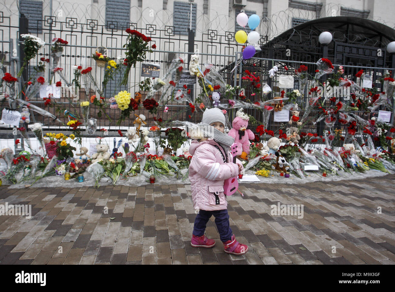 Kiev, Ukraine. 28th Mar, 2018. A little girl walks past near flowers and toys in memory for the victims of the fire in the shopping mall 'Zimnyaya Vishnya' in the West Siberian city of Kemerovo, in front the Russian Embassy in Kiev, Ukraine, on 28 March 2018. Reports state that at least 64 people, including 41 children, died in the fatal incident on 25 March. Credit: Serg Glovny/ZUMA Wire/Alamy Live News Stock Photo