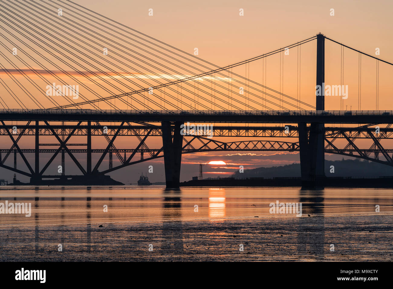 South Queensferry, Scotland, UK. 29th March, 2018. UK Weather: Beautiful sunrise on a clear cold morning behind the three famous bridges crossing the Firth of Forth at South Queensferry. The three bridges are the new Queensferry Crossing, Forth Road Bridge and the iconic Forth (rail) Bridge. Credit: Iain Masterton/Alamy Live News Stock Photo