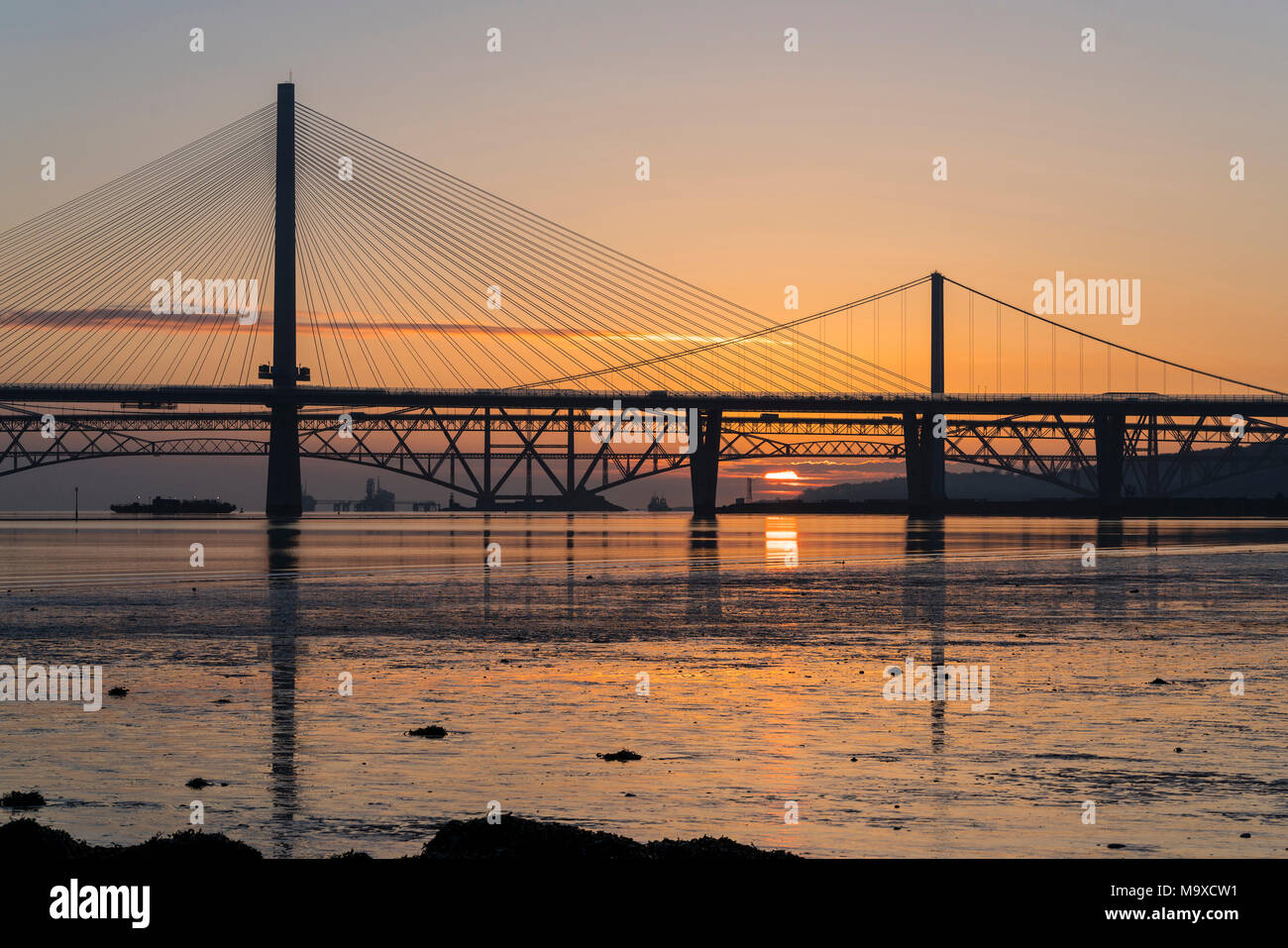 South Queensferry, Scotland, UK. 29th March, 2018. UK Weather: Beautiful sunrise on a clear cold morning behind the three famous bridges crossing the Firth of Forth at South Queensferry. The three bridges are the new Queensferry Crossing, Forth Road Bridge and the iconic Forth (rail) Bridge. Credit: Iain Masterton/Alamy Live News Stock Photo