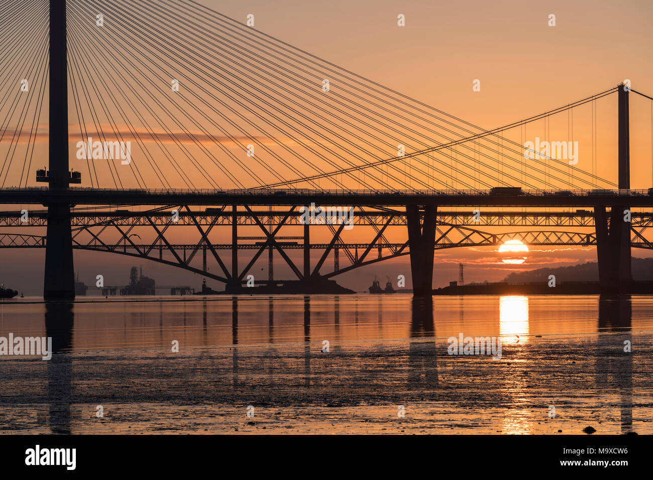 South Queensferry, Scotland, UK. 29th March, 2018. UK Weather: Beautiful sunrise on a clear cold morning behind the three famous bridges crossing the Firth of Forth at South Queensferry. The three bridges are the new Queensferry Crossing, Forth Road Bridge and the iconic Forth (rail) Bridge. Credit: Iain Masterton/Alamy Live News Stock Photo