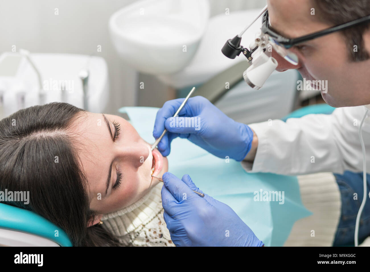 Dentist in magnifying glasses with lighting examines a patient teeth ...