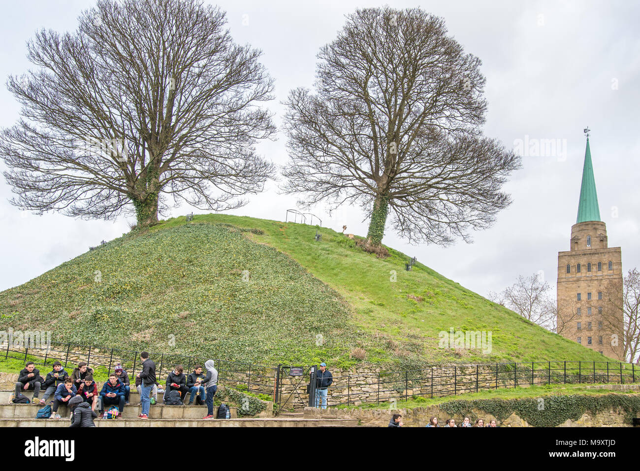 A group of tourist students eat lunch at the foot of the norman built mound (motte) of the castle in the town of Oxford, England, with the tower of th Stock Photo