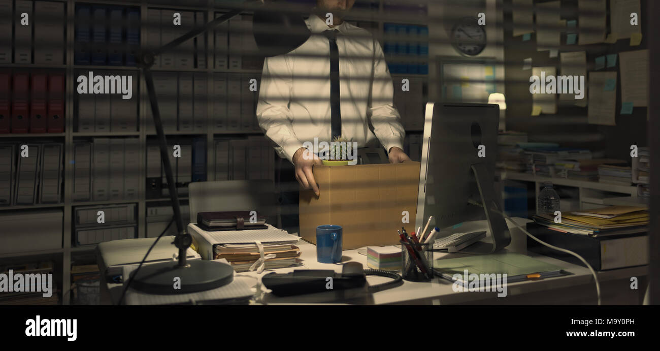 Sad office worker packing his belongings after being fired, he is holding a cardboard box Stock Photo