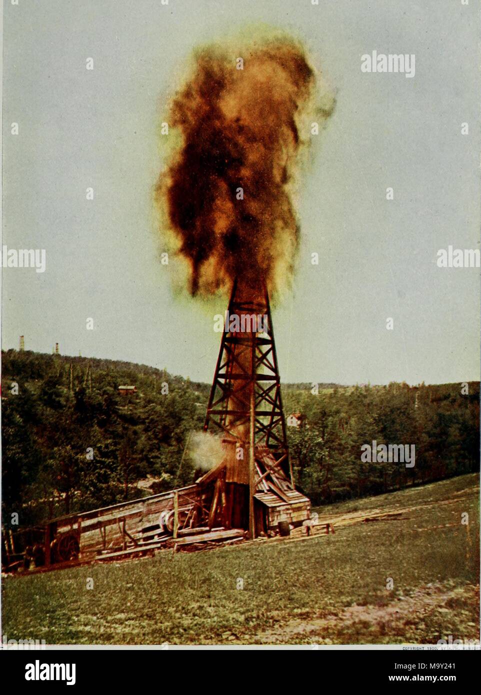 Color photograph depicting an oil well gushing or exploding above a wooden cabin-like structure, with a grassy rolling hill in the foreground, a pine forest, farm buildings, and other wells in the background, from the volume 'Nature neighbors, embracing birds, plants, animals, minerals, in natural colors by color photography' authored by Nathaniel Moore Banta, Albert Schneider, William Kerr Higley, and Gerard Alan Abbott, 1914. Courtesy Internet Archive. () Stock Photo
