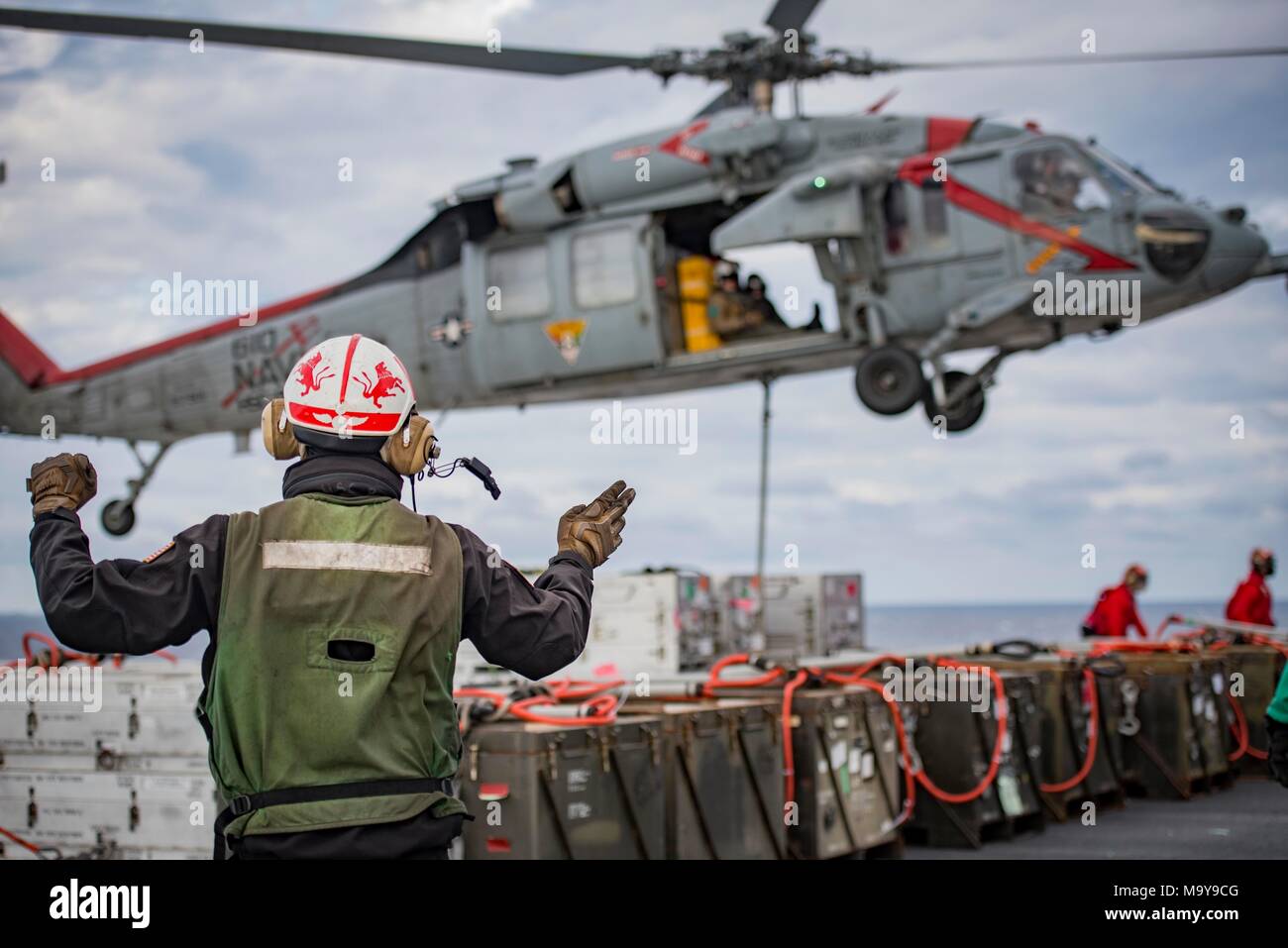 180326-N-SO730-0099 (March 26, 2018) Aviation Electrician's Mate 3rd Class Jacob Howell, from Sarasota, Florida, assigned to Helicopter Sea Combat Squadron 9, directs one of his squadron's MH-60S Sea Hawk helicopters during an ammunition offload aboard the aircraft carrier USS George H.W. Bush (CVN 77). The ship is underway conducting sustainment exercises to maintain carrier readiness. (U.S. Navy photo by Mass Communication Specialist 3rd Class Joe Boggio) Stock Photo