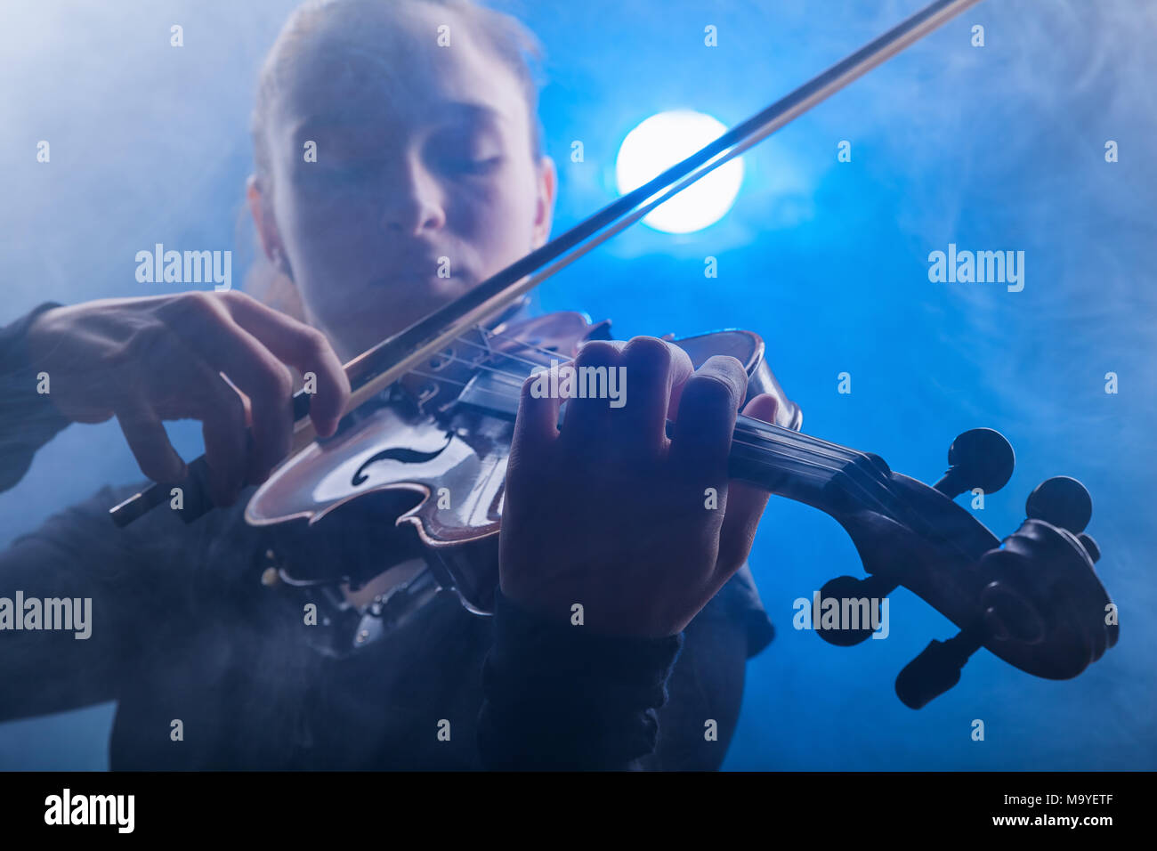 Woman playing the violin against a dark background. Fog in the background. Studio shot Stock Photo