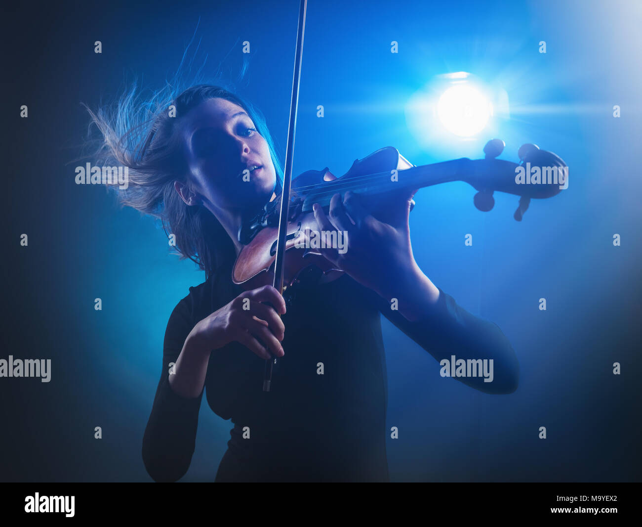 Beautiful young woman playing the violin with flying hair on a blue background. Studio shot Stock Photo