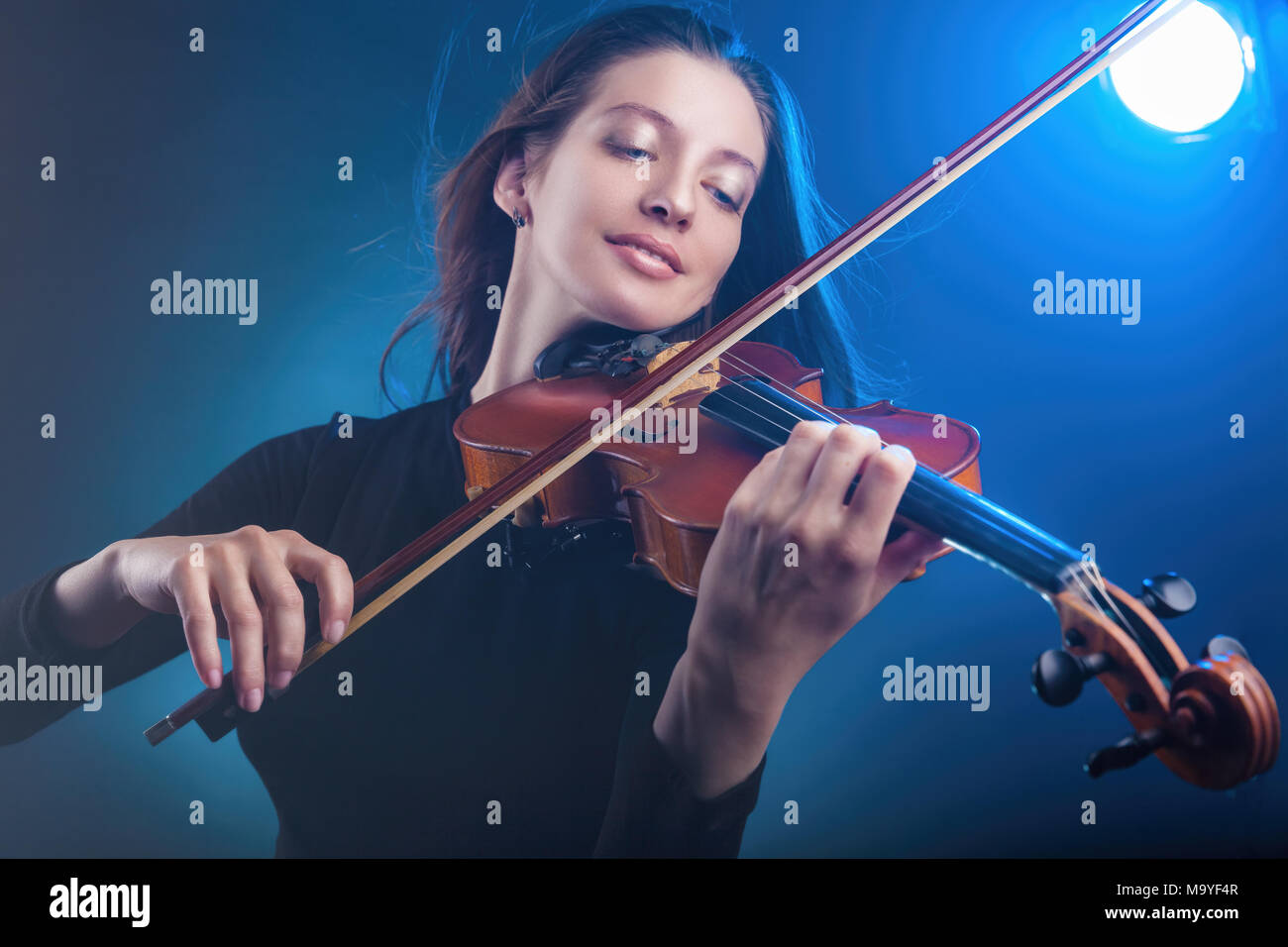 Beautiful young woman playing the violin on dark blue background. Studio shot Stock Photo