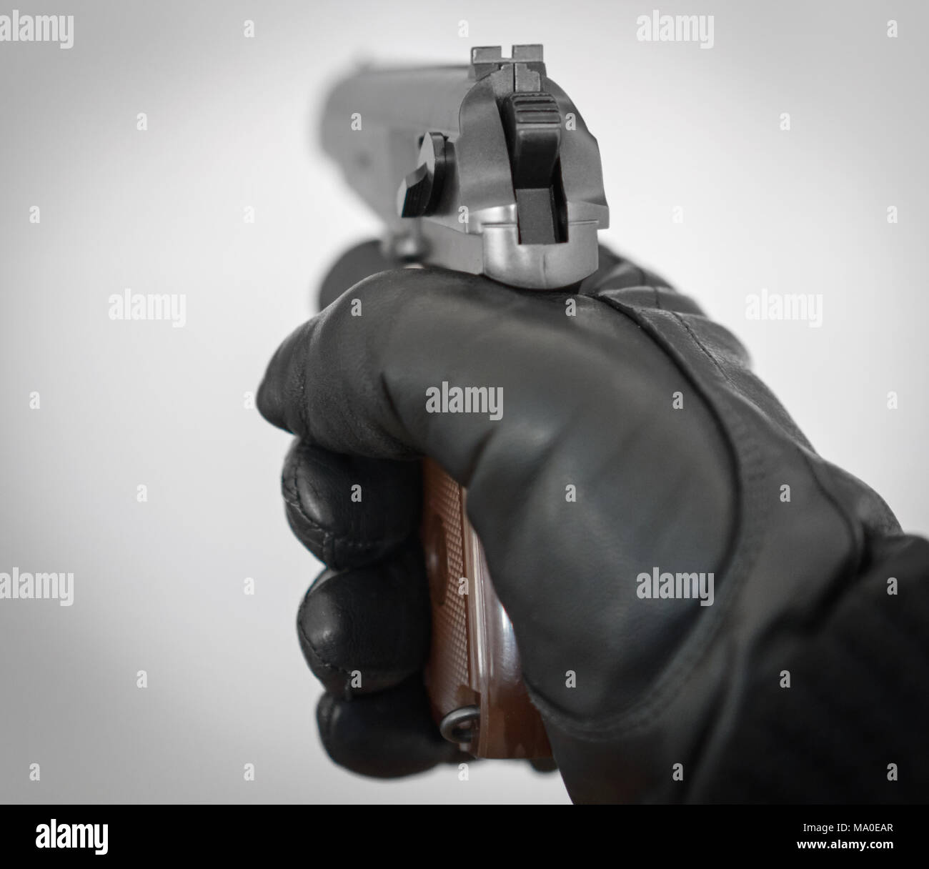 Hand in leather glove holding gun and aiming. Stock Photo