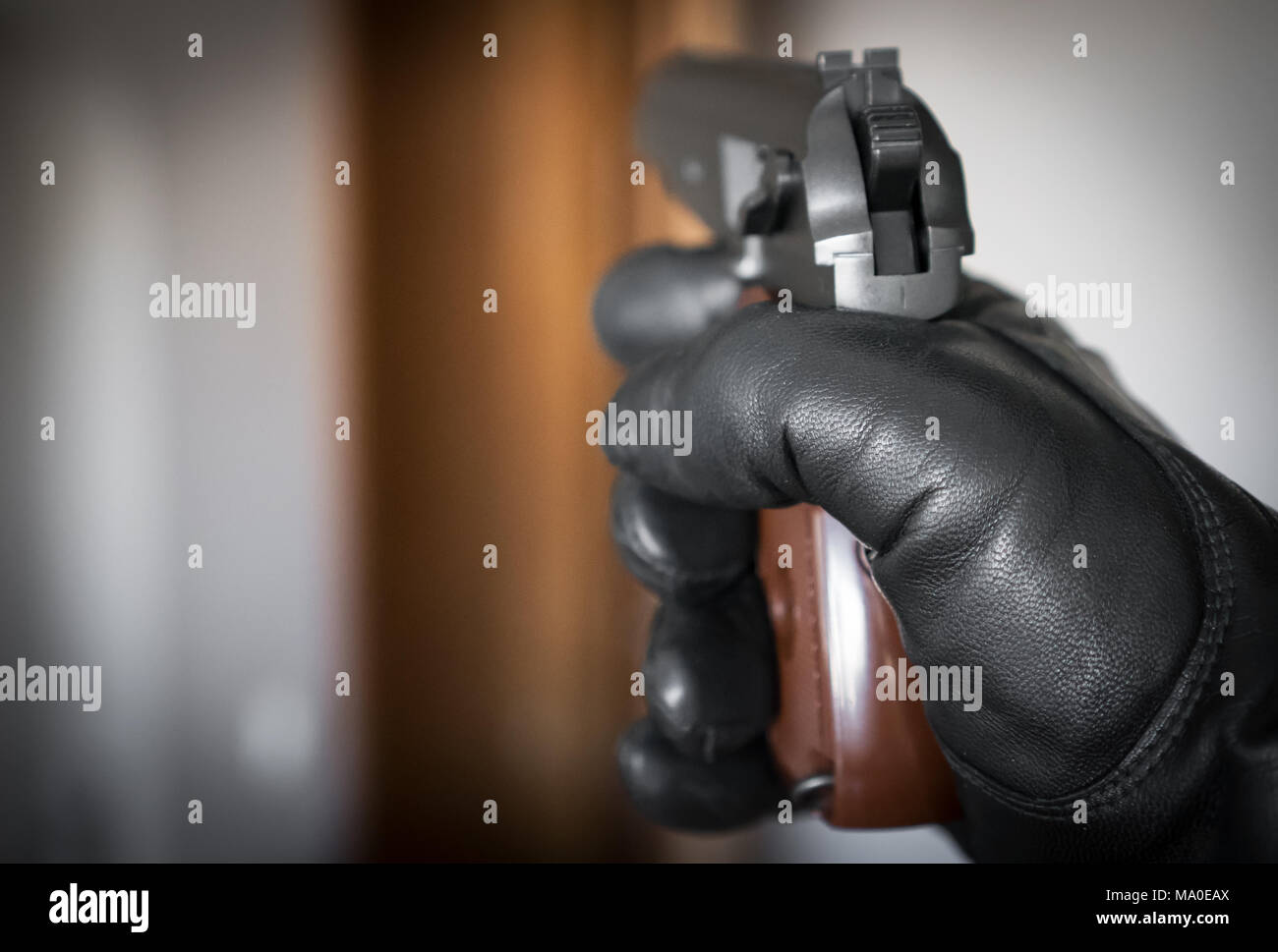 Hand in leather glove holding gun and aiming at the door. Stock Photo