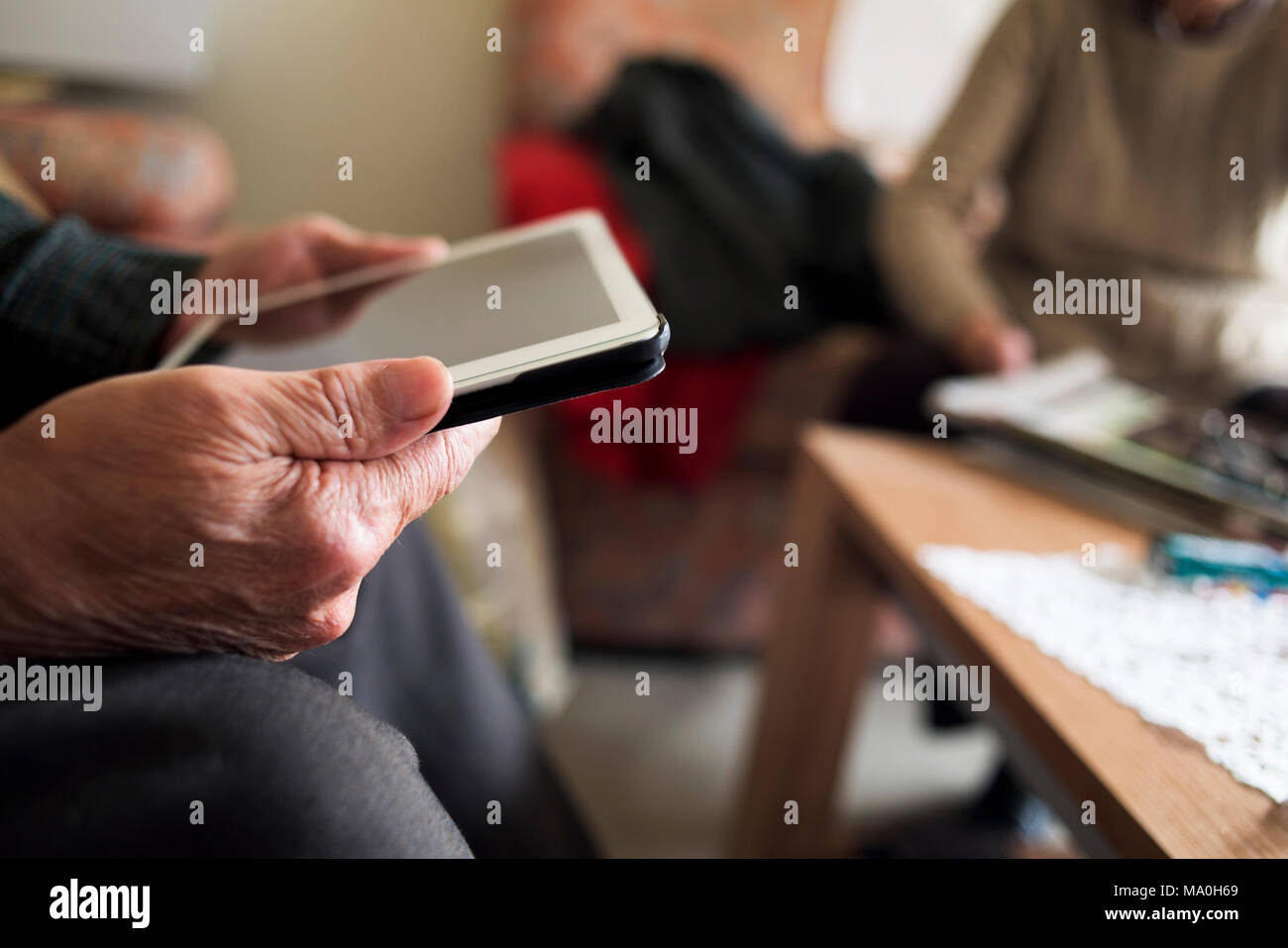 closeup of an old caucasian man using a tablet and an old caucasian man reading a magazine, sitting both in a couch Stock Photo