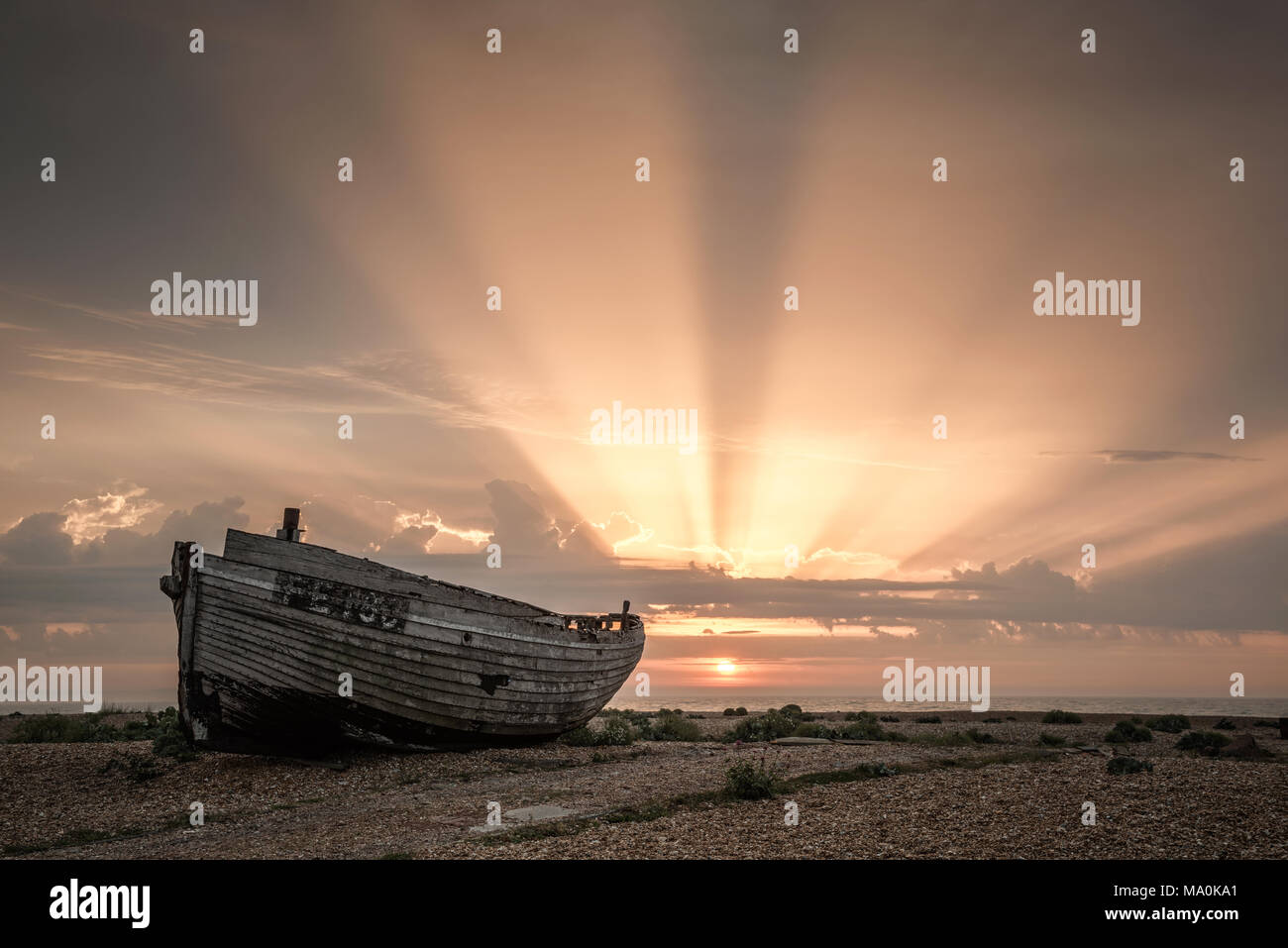 As the sun rises above the horizon at Dungeness in Kent the sky is filled with a beautiful sunburst, a fitting background to one of the many abandoned Stock Photo