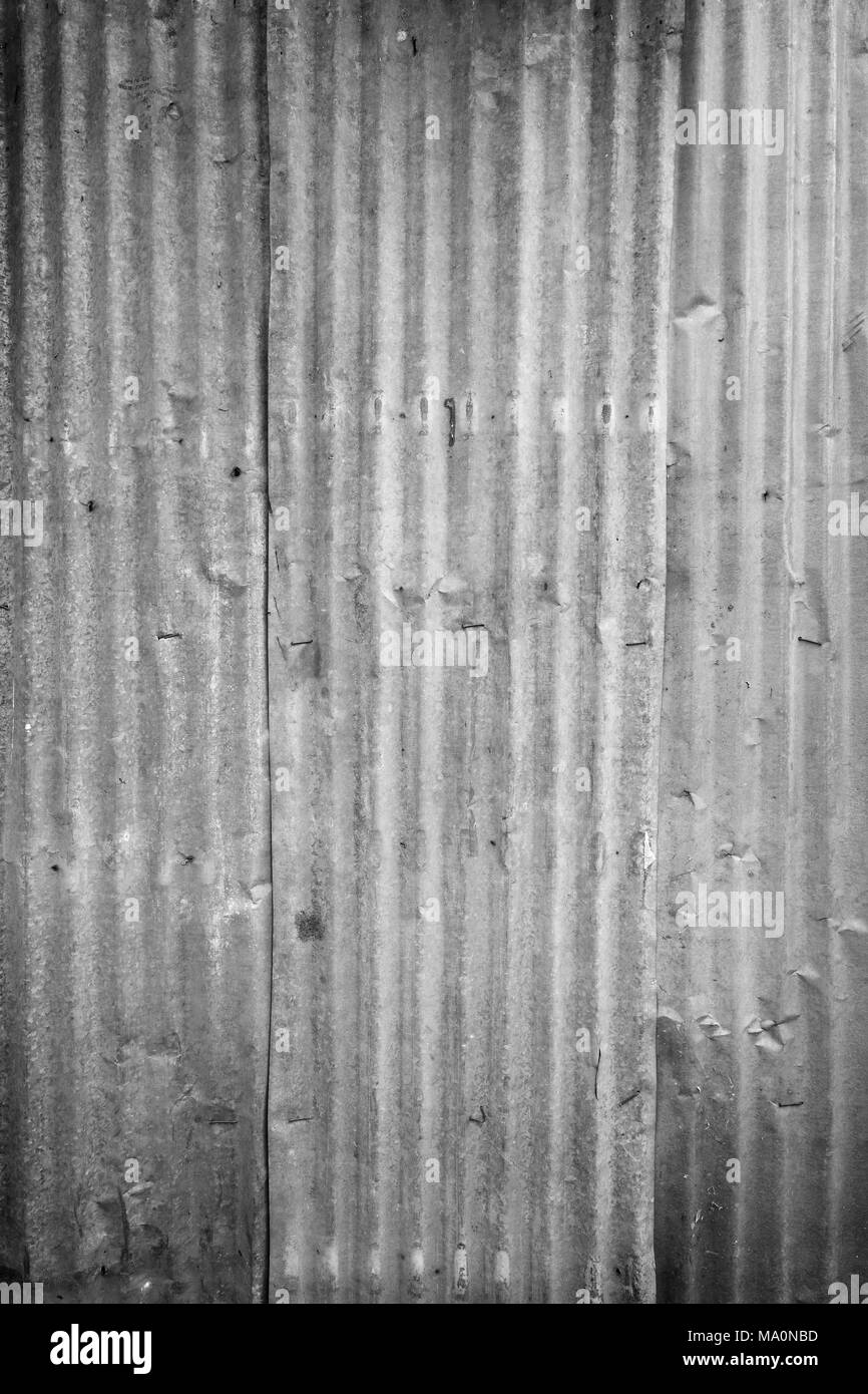 Faded and corrugated iron metal construction site wall texture background with vignette in black and white. Stock Photo