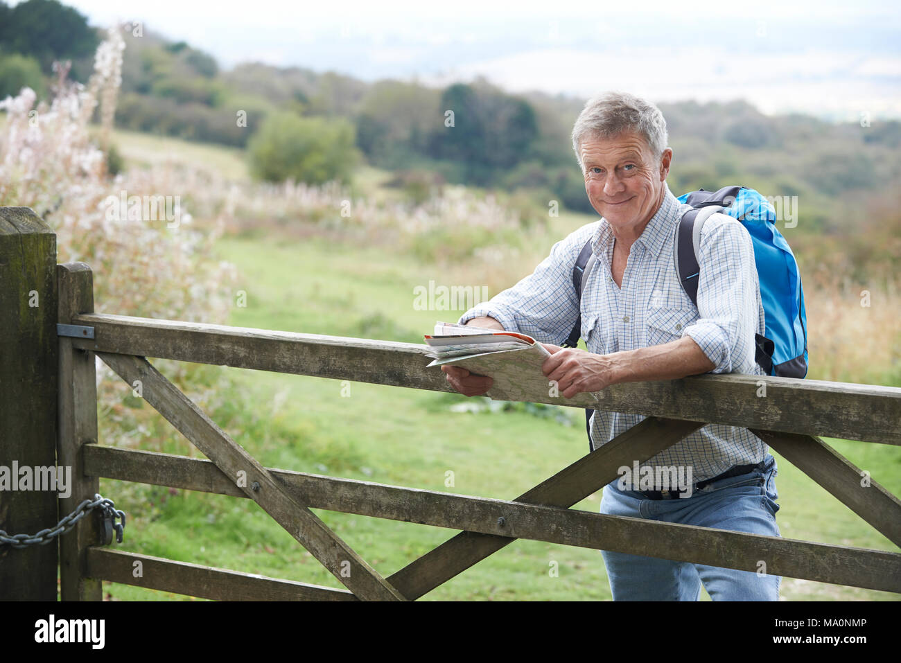 Portrait Of Senior Man With Map On Hike In Countryside Resting By Gate Stock Photo