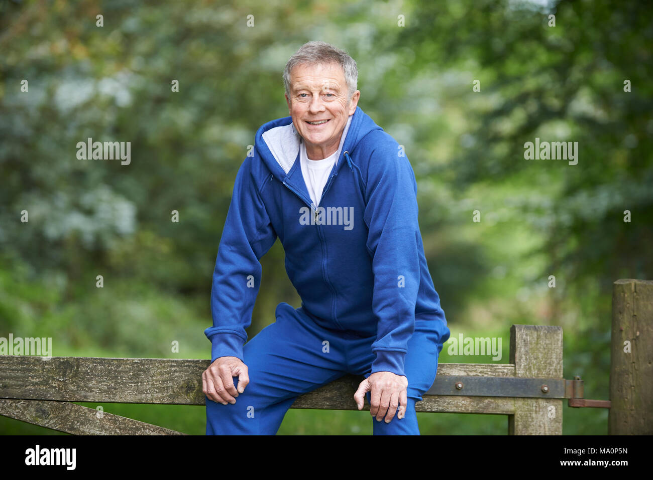 Senior Man Resting On Gate During Exercise In Countryside Stock Photo