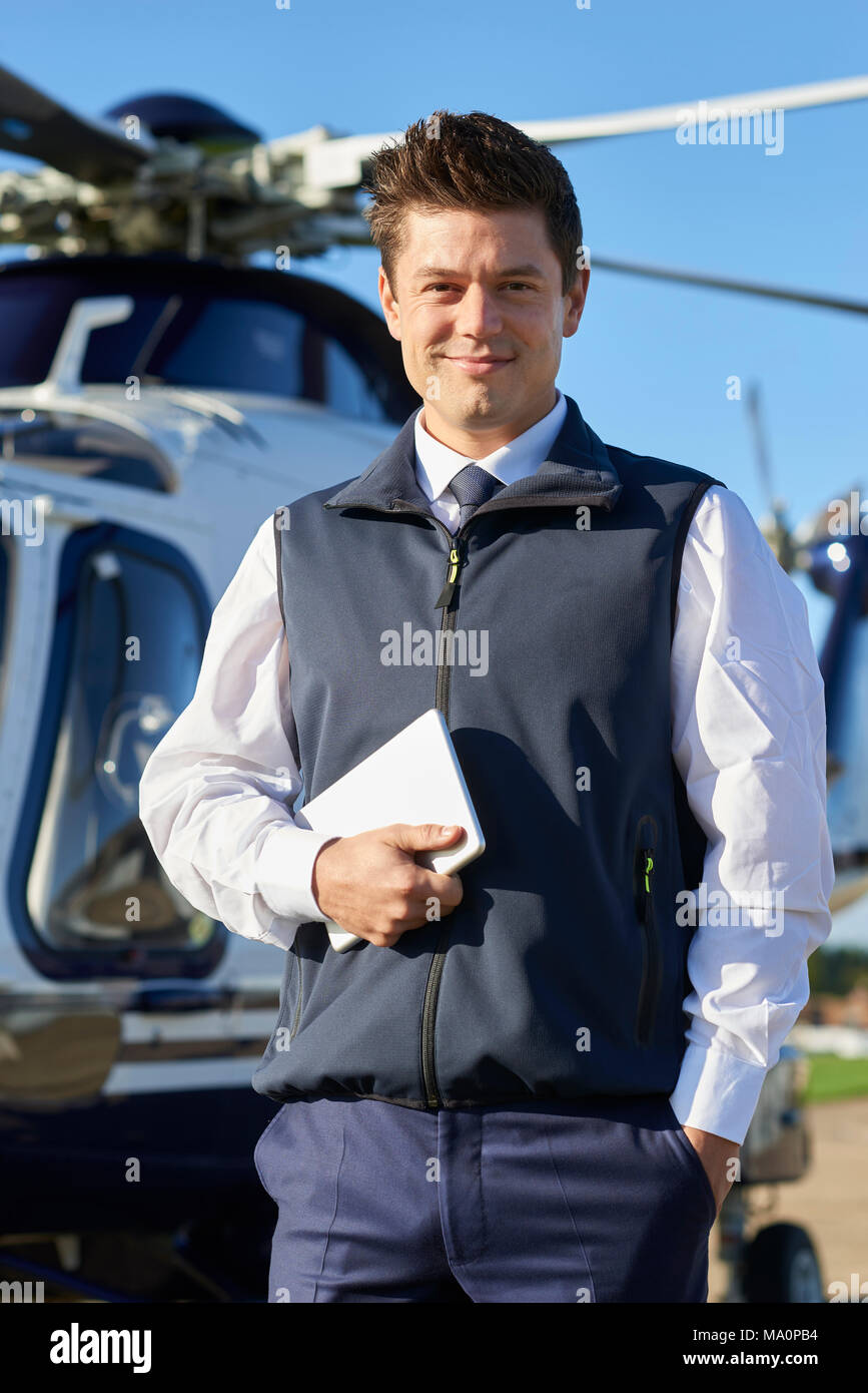 Portrait Of Smiling Pilot Standing In Front Of Helicopter With Digital Tablet Stock Photo