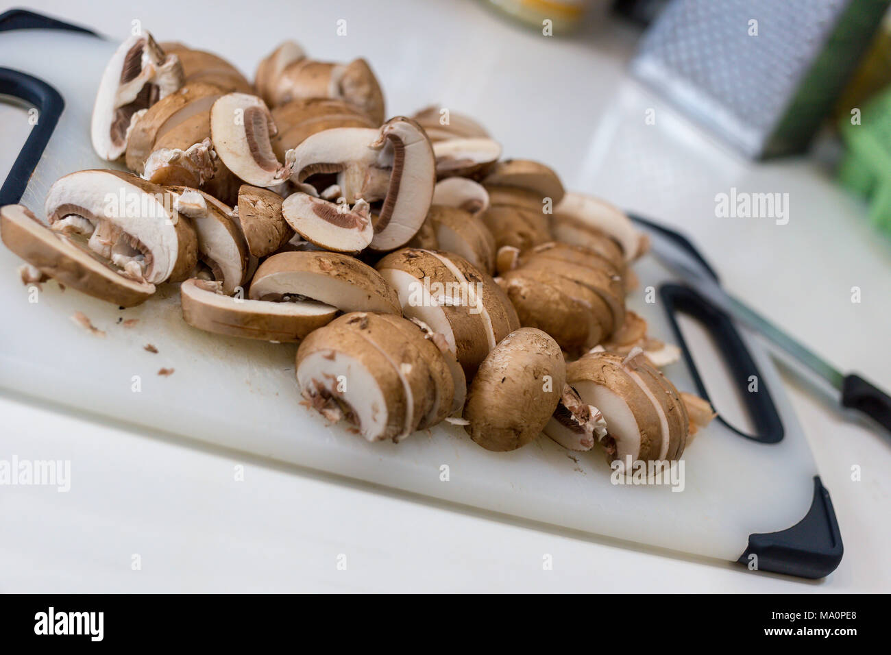 A pile of sliced chestnut mushrooms (Agaricus bisporus) on a white chopping board Stock Photo