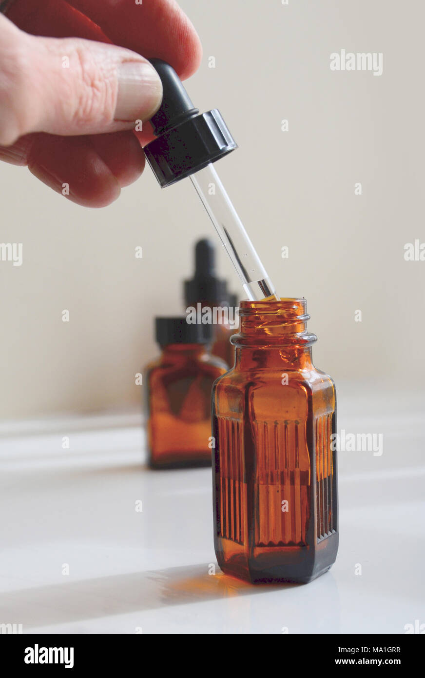 A person draws medicinal oil up a pipette from an amber bottle. Stock Photo