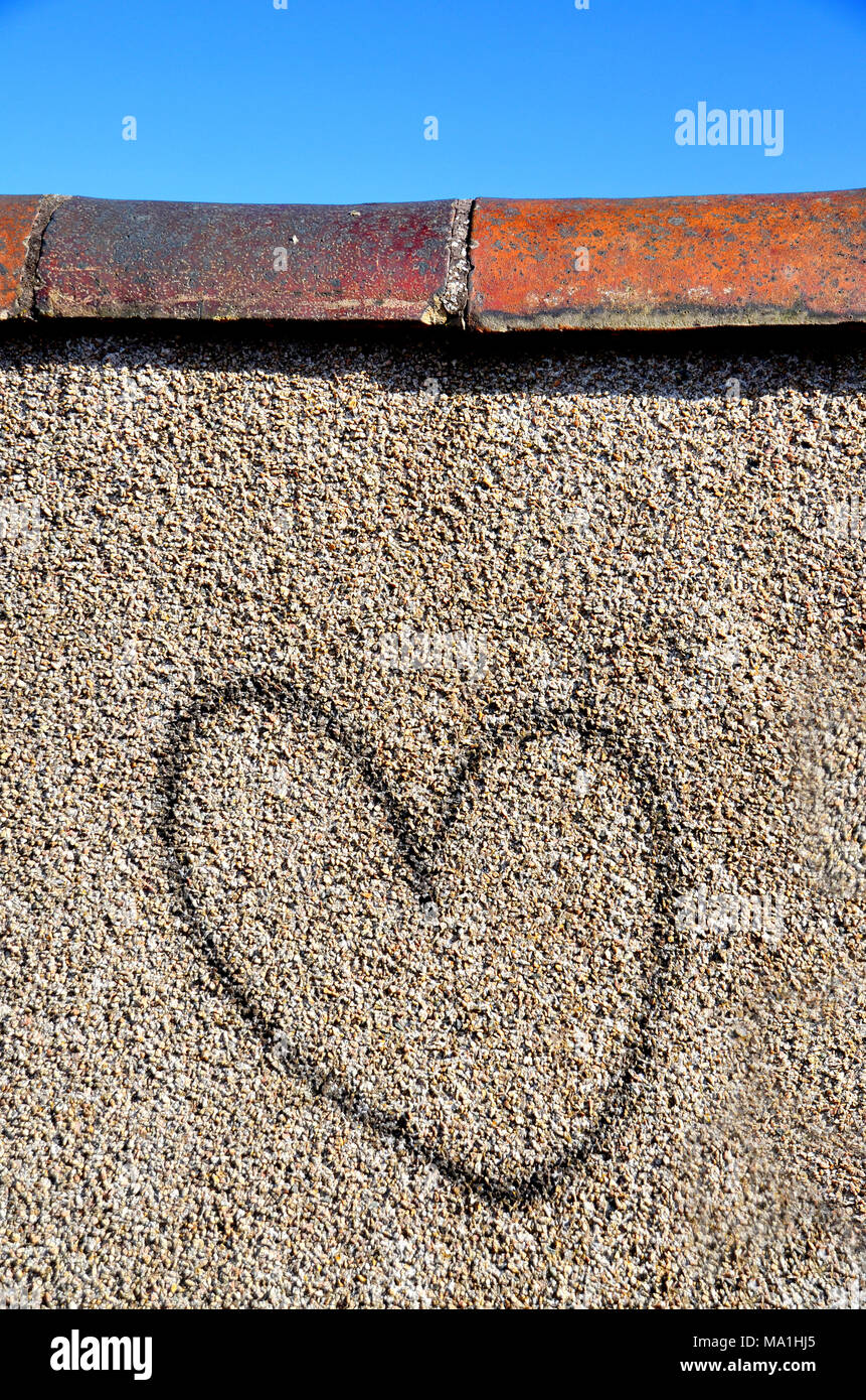 A pebble dashed wall with a graffiti black heart Stock Photo