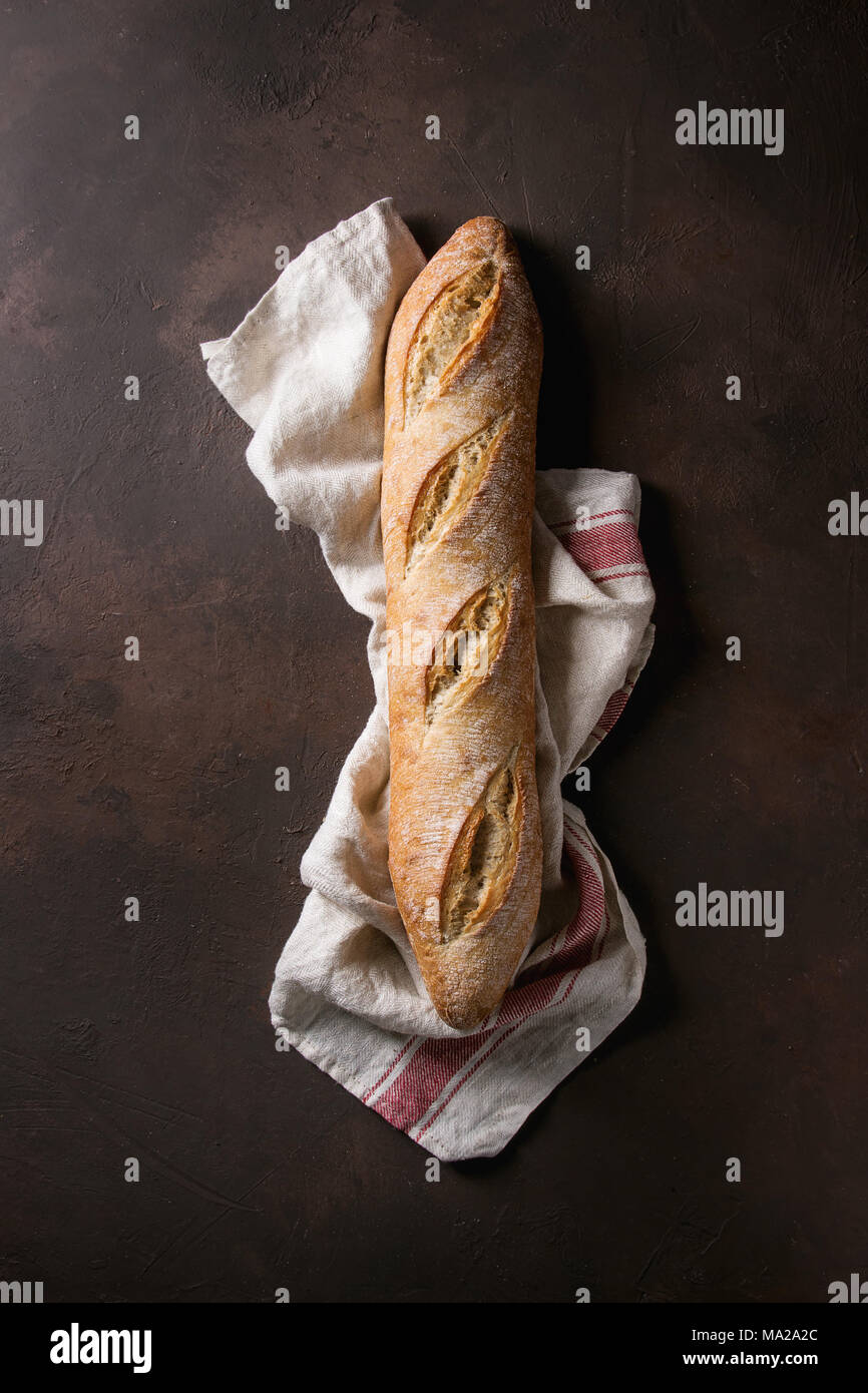 Loaf of fresh baked artisan baguette bread on linen cloth over dark ...