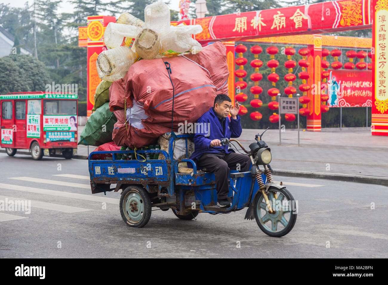 Luoyang, China - 7 March 2018 - Chinese man rides his three wheeled motorbike truck carrying lots of containers on a street of Luoyang, China on March Stock Photo