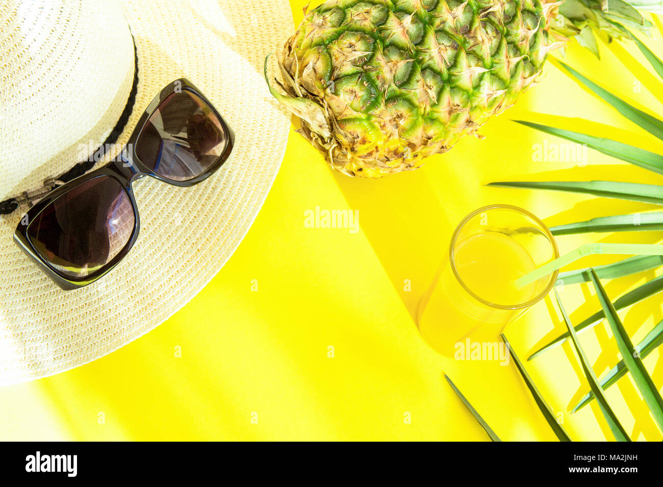 Elegant Woman Accessories Hat Sunglasses Tall Glass with Fresh Citrus Tropical Fruit Juice Pineapple Palm Leaves on Yellow Background. Sunlight Leaks. Stock Photo