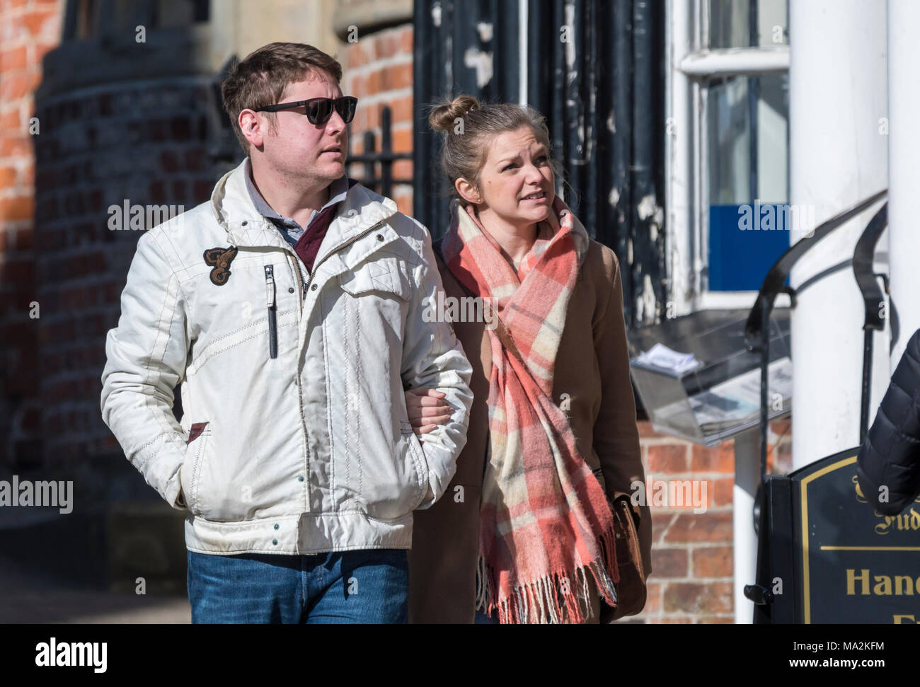 Young couple dressed in warm clothes walking through a small town linking arms in Winter in the UK. Stock Photo