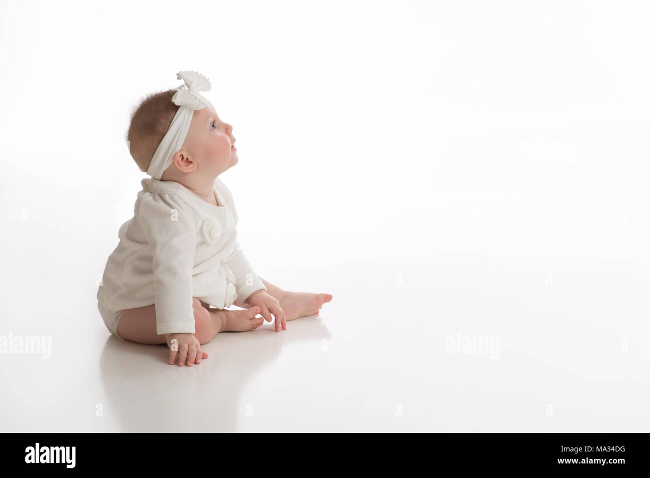 A profile view of a smiling, seven month old, baby girl wearing white. Shot in the studio on a white, seamless backdrop. Stock Photo